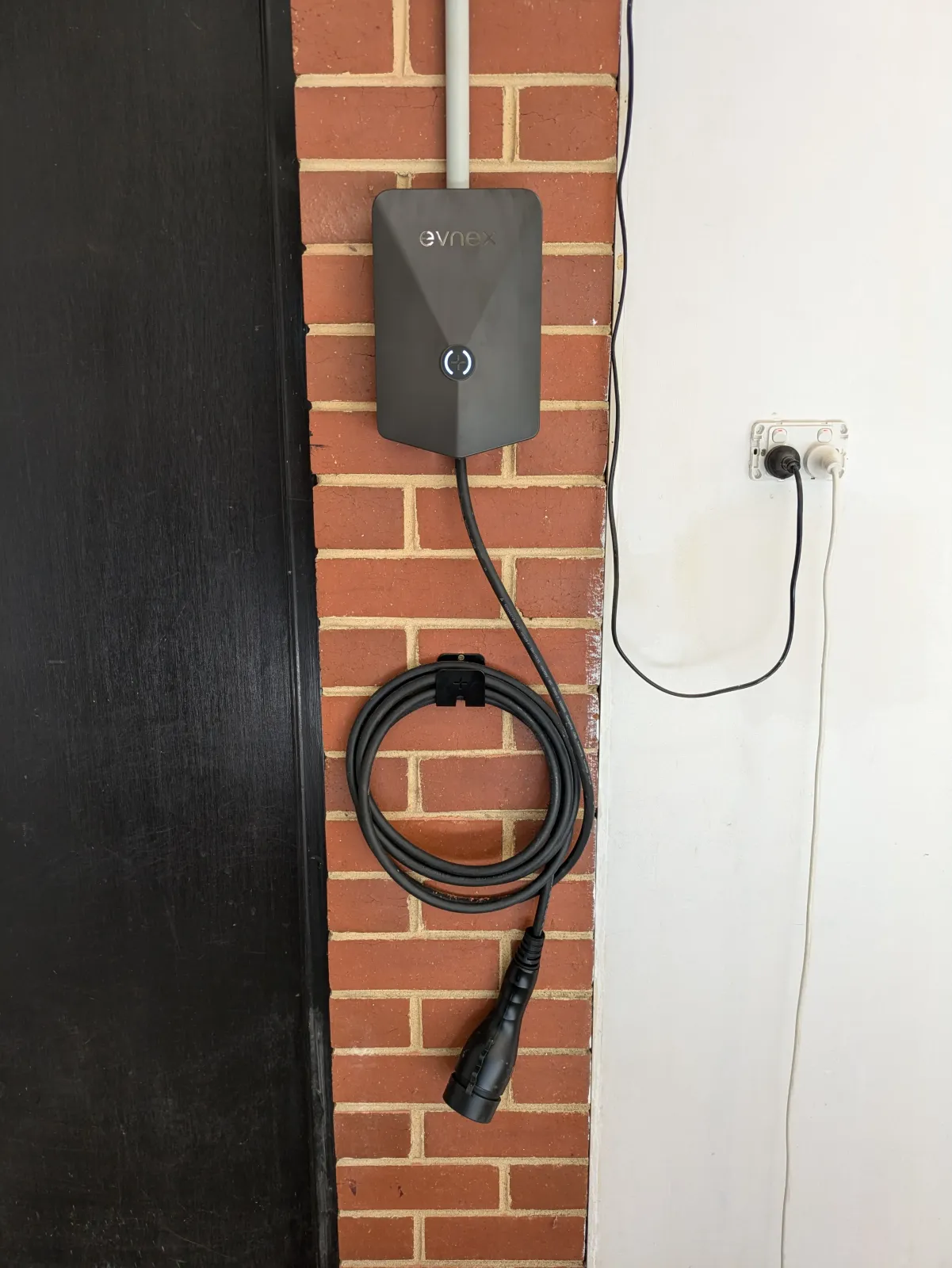 An Evnex EV charger on a brick wall with the cable holstered