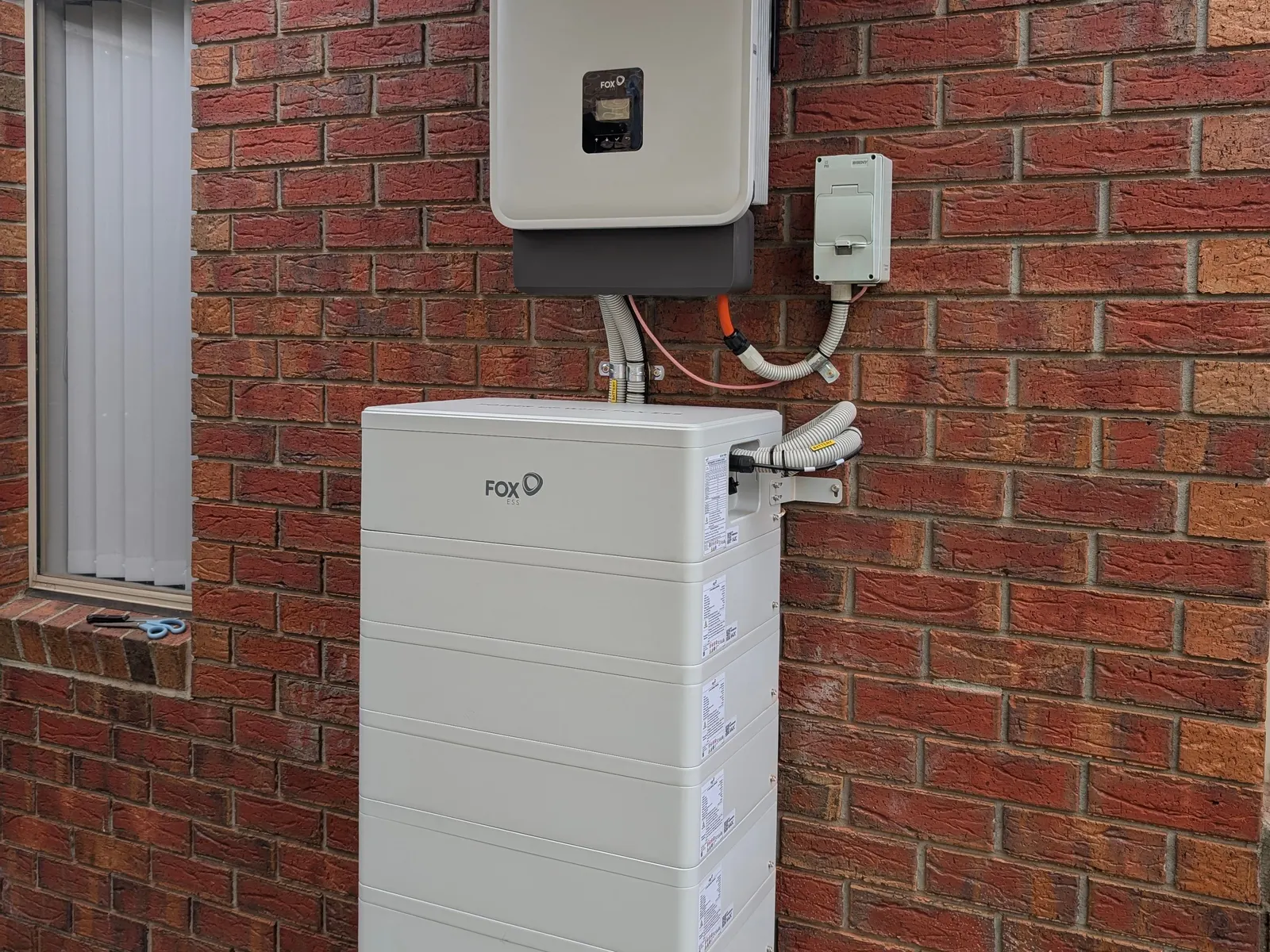 Fox ESS battery and inverter on a brick wall, sited under the eave
