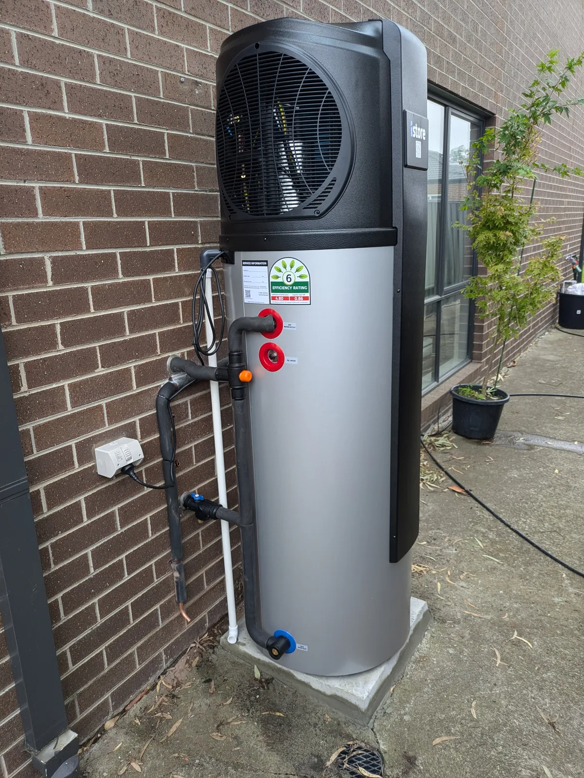 An iStore heat pump installed against a brick wall, its efficiency label showing a COP of 4.80